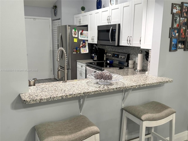 5928 NW 93rd Ter, Tamarac, FL 33321 - kitchen with appliances with stainless steel finishes, tasteful backsplash, white cabinets, a kitchen breakfast bar, and light stone countertops