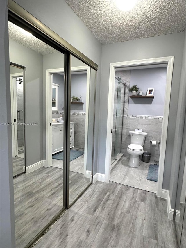 5928 NW 93rd Ter, Tamarac, FL 33321 - bathroom featuring wood finished floors, a stall shower, a textured ceiling, and tile walls