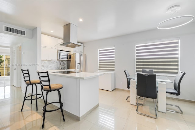 471 Capri J Unit 471, Delray Beach, FL 33484 - kitchen featuring stainless steel appliances, island range hood, white cabinets, a kitchen breakfast bar, and decorative backsplash