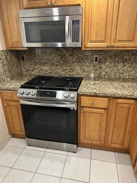 720 Collins Ave Unit 310, Miami Beach, FL 33139 - kitchen with stainless steel appliances, light stone counters, decorative backsplash, and brown cabinets