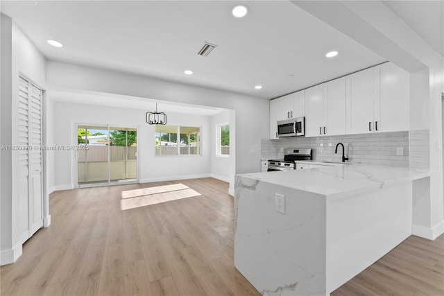 7021 SW 12th St, Pembroke Pines, FL 33023 - kitchen with stainless steel appliances, white cabinets, backsplash, light stone counters, and light wood-type flooring