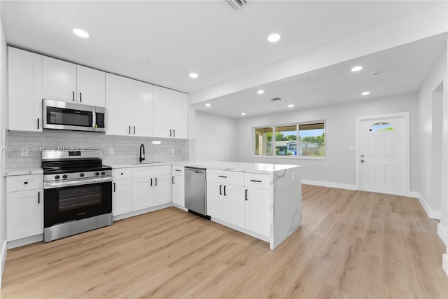 7021 SW 12th St, Pembroke Pines, FL 33023 - kitchen with stainless steel appliances, a peninsula, light wood-style flooring, tasteful backsplash, and white cabinets