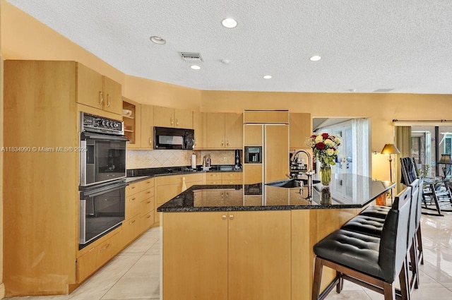 9940 SW 4th St, Plantation, FL 33324 - kitchen featuring black appliances, light brown cabinetry, a textured ceiling, decorative backsplash, and a kitchen island with sink