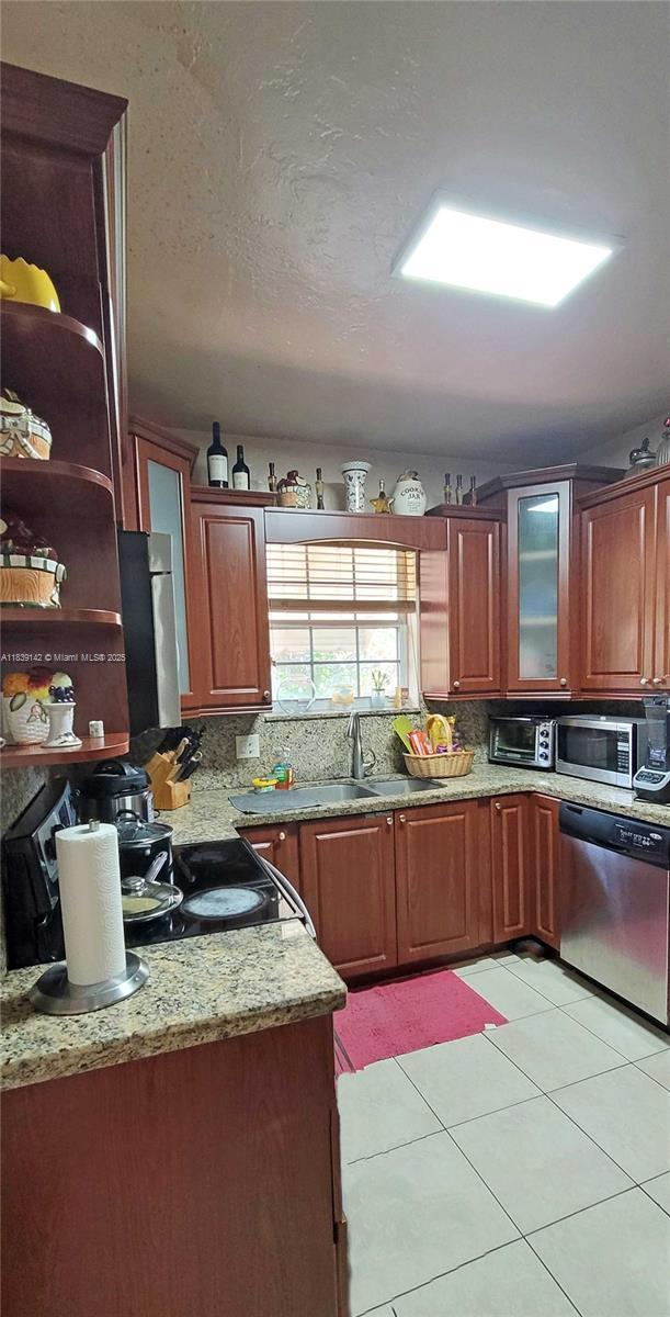 1824 SW 24th St, Miami, FL 33145 - kitchen with appliances with stainless steel finishes, light stone counters, light tile patterned floors, glass insert cabinets, and brown cabinetry