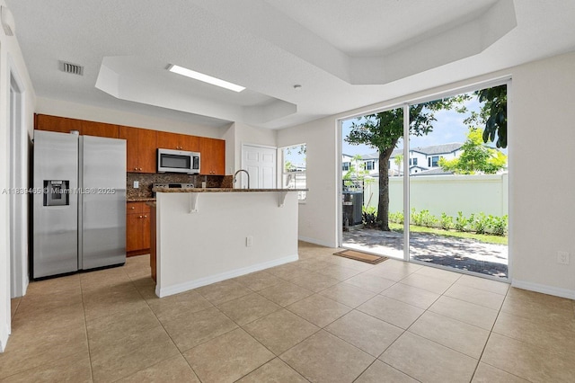 3066 S Red Mangrove Ln S Unit 201-2, Dania Beach, FL 33312 - kitchen with appliances with stainless steel finishes, a raised ceiling, decorative backsplash, brown cabinets, and a kitchen bar
