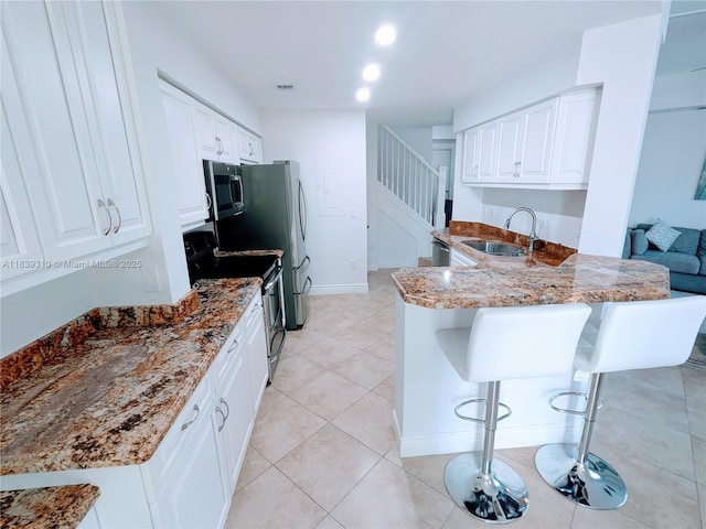 1900 Oceanwalk Ln Unit 123, Lauderdale By The Sea, FL 33062 - kitchen featuring appliances with stainless steel finishes, white cabinetry, light stone countertops, and a breakfast bar area