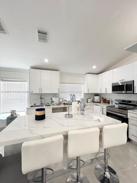 4966 SW 33rd Ter, Hollywood, FL 33312 - kitchen featuring backsplash, stainless steel microwave, a kitchen bar, light stone countertops, and crown molding