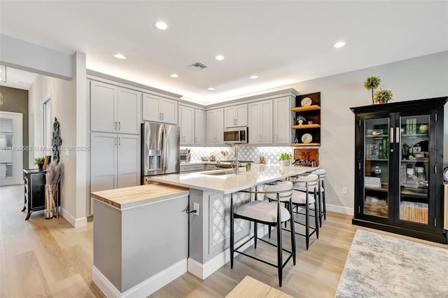 15734 SW Egret Coast Dr, Port St Lucie, FL 34987 - kitchen featuring appliances with stainless steel finishes, open shelves, light wood-style floors, a breakfast bar area, and a peninsula