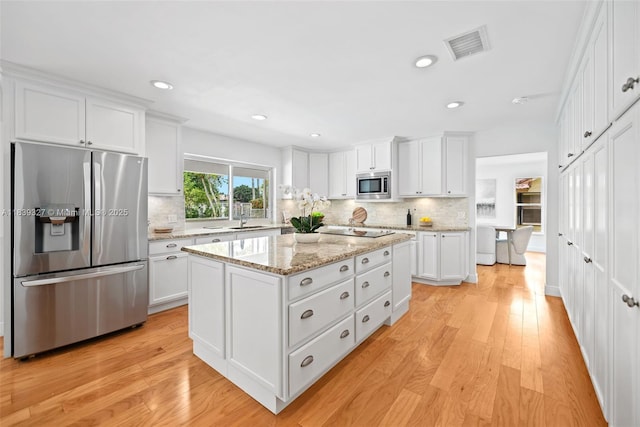 7545 Banyan Way, Tamarac, FL 33321 - kitchen featuring stainless steel appliances, white cabinetry, tasteful backsplash, a kitchen island, and light wood finished floors