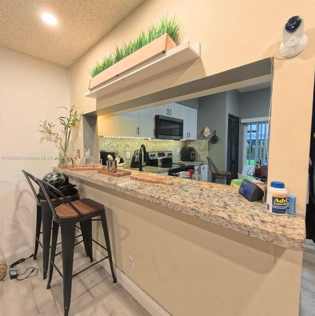 16652 Hemingway Dr, Weston, FL 33326 - kitchen with appliances with stainless steel finishes, tasteful backsplash, a peninsula, light wood finished floors, and a kitchen bar