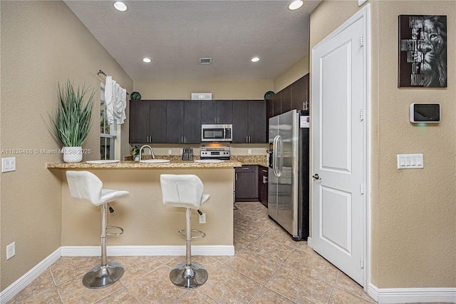 10608 NW 36th St, Coral Springs, FL 33065 - kitchen with stainless steel appliances, a peninsula, a kitchen breakfast bar, light tile patterned floors, and a textured wall