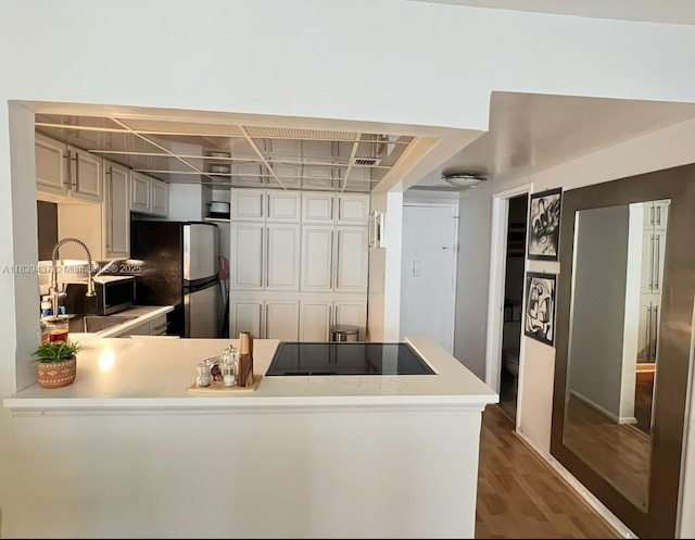 1228 W Ave Unit 911, Miami Beach, FL 33139 - kitchen with freestanding refrigerator, black electric stovetop, light countertops, dark wood-style flooring, and a peninsula