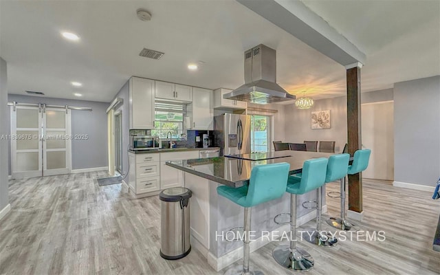 2359 Gabriel Ln, West Palm Beach, FL 33406 - kitchen featuring island exhaust hood, stainless steel refrigerator with ice dispenser, light wood finished floors, a kitchen bar, and white cabinets
