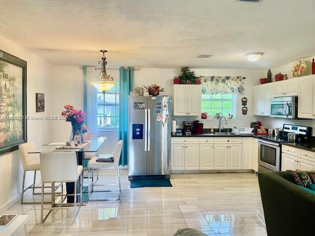 140 NW 199th St, Miami Gardens, FL 33169 - kitchen featuring appliances with stainless steel finishes, dark countertops, white cabinetry, and hanging light fixtures