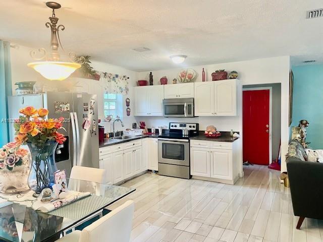 140 NW 199th St, Miami Gardens, FL 33169 - kitchen featuring appliances with stainless steel finishes, dark countertops, white cabinets, and decorative light fixtures