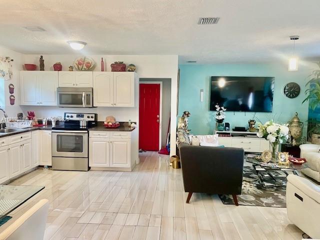 140 NW 199th St, Miami Gardens, FL 33169 - kitchen featuring stainless steel appliances, dark countertops, white cabinetry, and light wood-style floors