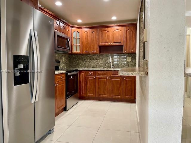 330 W 40th Pl, Hialeah, FL 33012 - kitchen with appliances with stainless steel finishes, tasteful backsplash, glass insert cabinets, recessed lighting, and light tile patterned floors