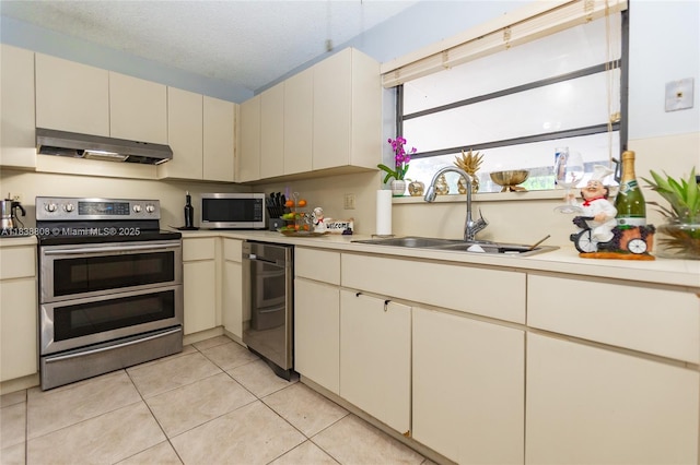 906 Cardinal Pl, Homestead, FL 33035 - kitchen featuring stainless steel appliances, cream cabinetry, under cabinet range hood, light tile patterned floors, and light countertops