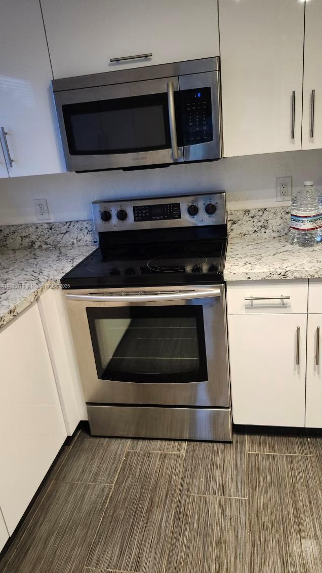 2501 NW 41st Ave Unit 201, Lauderhill, FL 33313 - kitchen with appliances with stainless steel finishes, white cabinets, and light stone counters