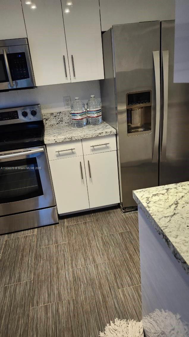 2501 NW 41st Ave Unit 201, Lauderhill, FL 33313 - kitchen with stainless steel appliances, white cabinetry, and light stone countertops