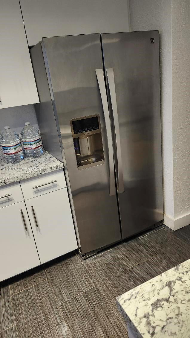 2501 NW 41st Ave Unit 201, Lauderhill, FL 33313 - kitchen featuring stainless steel refrigerator with ice dispenser, white cabinetry, light stone countertops, a textured wall, and dark wood-style floors