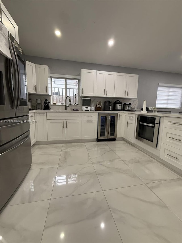 3134 W 70th Ter, Hialeah, FL 33018 - kitchen with oven, refrigerator with ice dispenser, wine cooler, white cabinetry, and light marble finish floors
