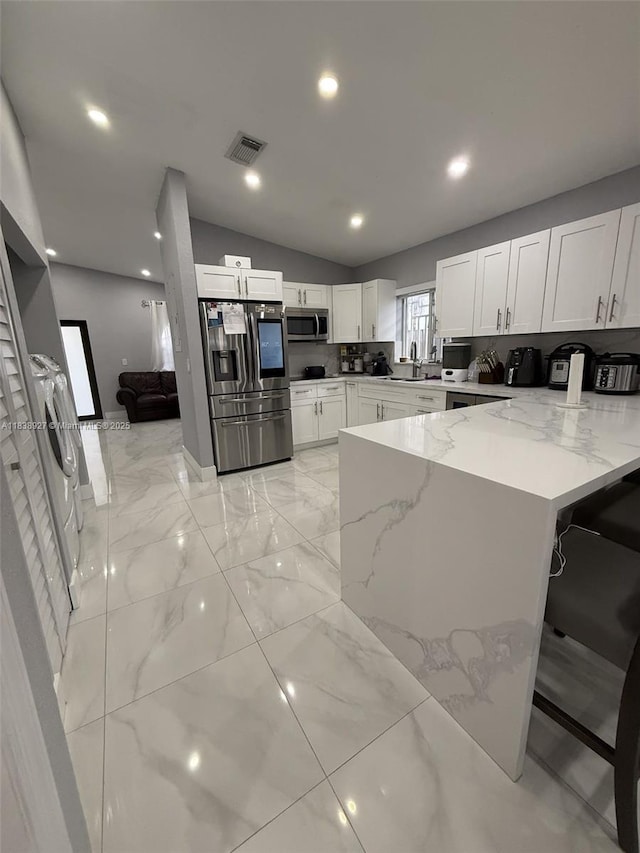 3134 W 70th Ter, Hialeah, FL 33018 - kitchen with appliances with stainless steel finishes, a peninsula, light stone counters, white cabinets, and lofted ceiling