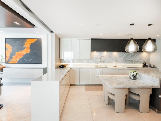 17475 Collins Ave Unit 1001, Sunny Isles Beach, FL 33160 - kitchen featuring modern cabinets, backsplash, decorative light fixtures, white cabinets, and light stone counters