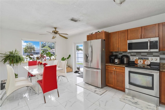 231 E 41st St, Hialeah, FL 33013 - kitchen with stainless steel appliances, brown cabinetry, ceiling fan, light marble finish flooring, and a textured ceiling