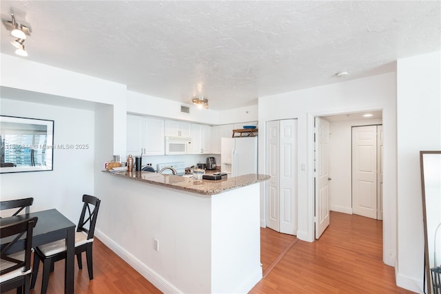 1155 Brickell Bay Dr Unit 3403, Miami, FL 33131 - kitchen featuring white appliances, light wood-type flooring, a peninsula, white cabinets, and light stone countertops