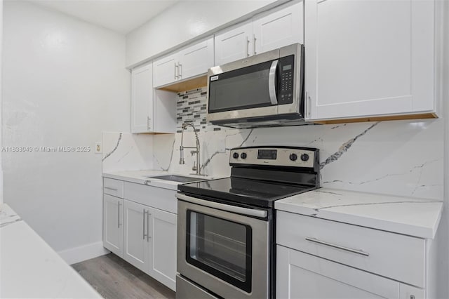 15900 NW 18th Ave, Miami Gardens, FL 33054 - kitchen featuring stainless steel appliances, decorative backsplash, white cabinetry, light wood finished floors, and light stone countertops