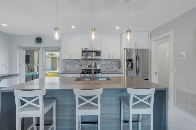11940 NW 33rd St, Sunrise, FL 33323 - kitchen featuring stainless steel appliances, backsplash, white cabinetry, an island with sink, and hanging light fixtures