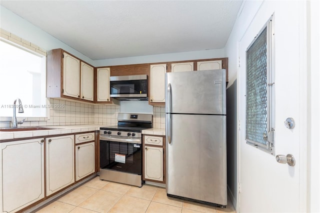 3551 NE 169th St Unit 411, North Miami Beach, FL 33160 - kitchen with appliances with stainless steel finishes, tile countertops, backsplash, and light tile patterned flooring