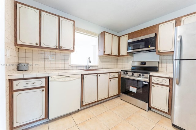3551 NE 169th St Unit 411, North Miami Beach, FL 33160 - kitchen featuring appliances with stainless steel finishes, decorative backsplash, tile countertops, and light tile patterned flooring