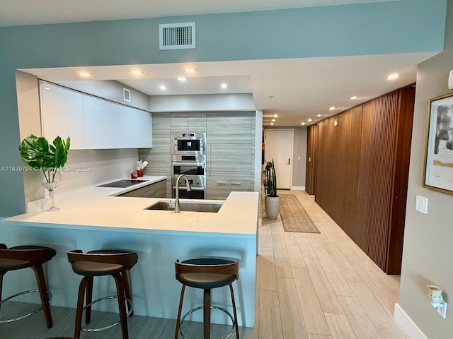 300 Sunny Isles Blvd Unit 4-1806, Sunny Isles Beach, FL 33160 - kitchen with black electric stovetop, a peninsula, light wood-type flooring, a breakfast bar, and modern cabinets