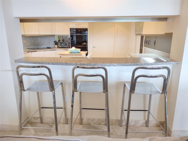 445 Grand Bay Dr Unit 601, Key Biscayne, FL 33149 - kitchen featuring black appliances, decorative backsplash, light stone countertops, and cream cabinetry