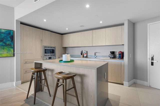 4111 S Ocean Dr Unit 2906, Hollywood, FL 33019 - kitchen featuring stainless steel microwave, light brown cabinetry, light countertops, a kitchen bar, and a kitchen island