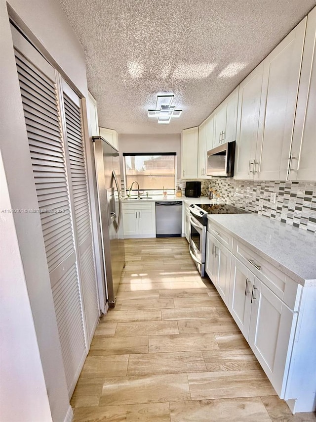 6169 NW 170th Ter, Hialeah, FL 33015 - kitchen with appliances with stainless steel finishes, white cabinetry, light wood-style floors, tasteful backsplash, and a textured ceiling