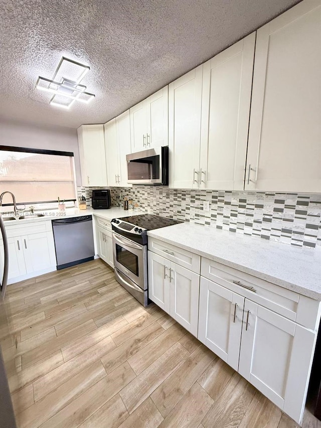 6169 NW 170th Ter, Hialeah, FL 33015 - kitchen featuring appliances with stainless steel finishes, white cabinetry, light wood-type flooring, backsplash, and a textured ceiling