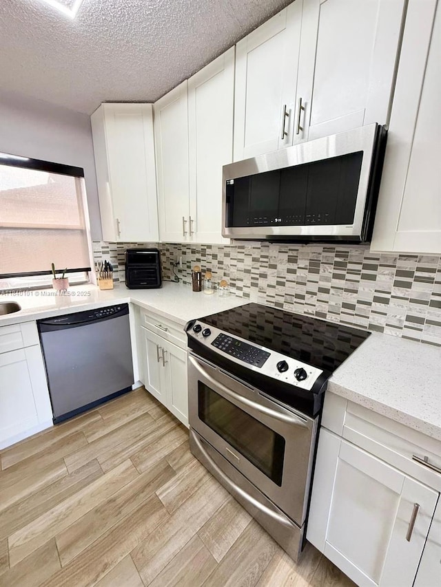 6169 NW 170th Ter, Hialeah, FL 33015 - kitchen with appliances with stainless steel finishes, white cabinetry, light wood-type flooring, a textured ceiling, and backsplash