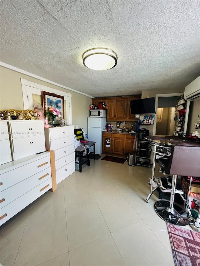 180 E 46th St, Hialeah, FL 33013 - kitchen featuring freestanding refrigerator, brown cabinetry, light tile patterned floors, a textured ceiling, and an AC wall unit
