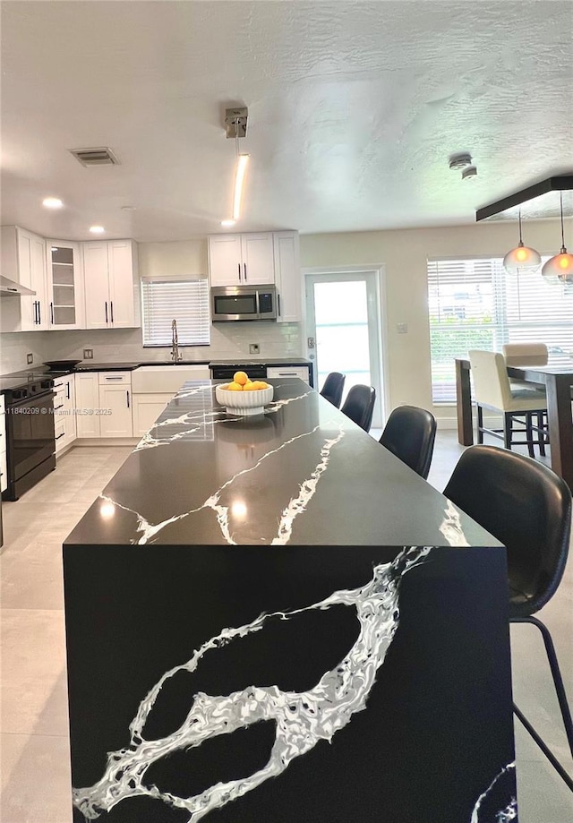 9130 SW 17th Ter, Miami, FL 33165 - kitchen with stainless steel microwave, dark countertops, white cabinetry, glass insert cabinets, and black / electric stove