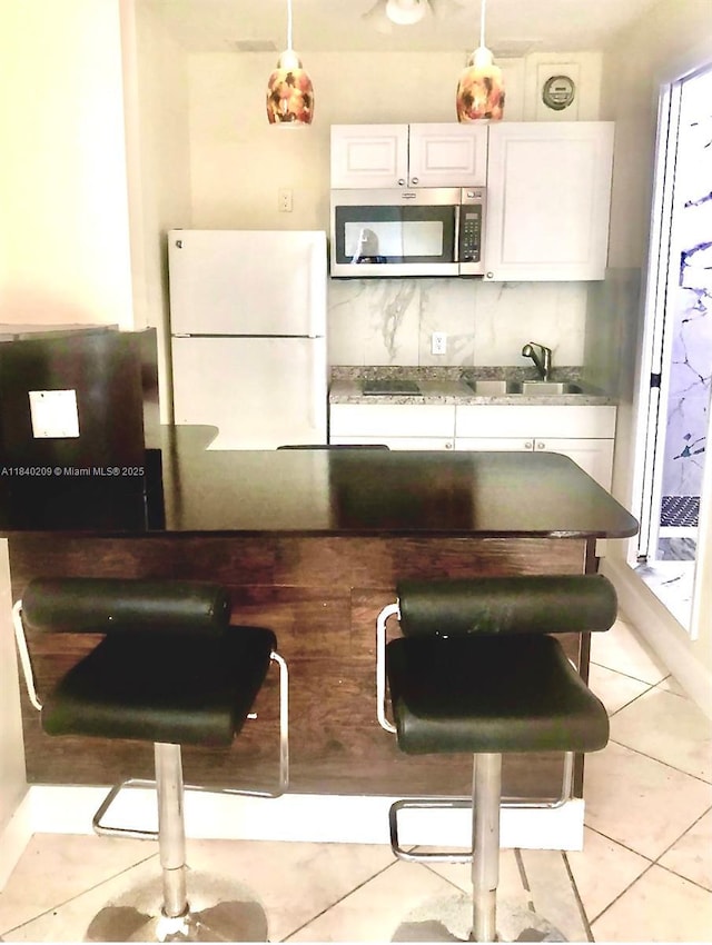 9130 SW 17th Ter, Miami, FL 33165 - kitchen with stainless steel microwave, freestanding refrigerator, white cabinetry, tasteful backsplash, and light tile patterned flooring