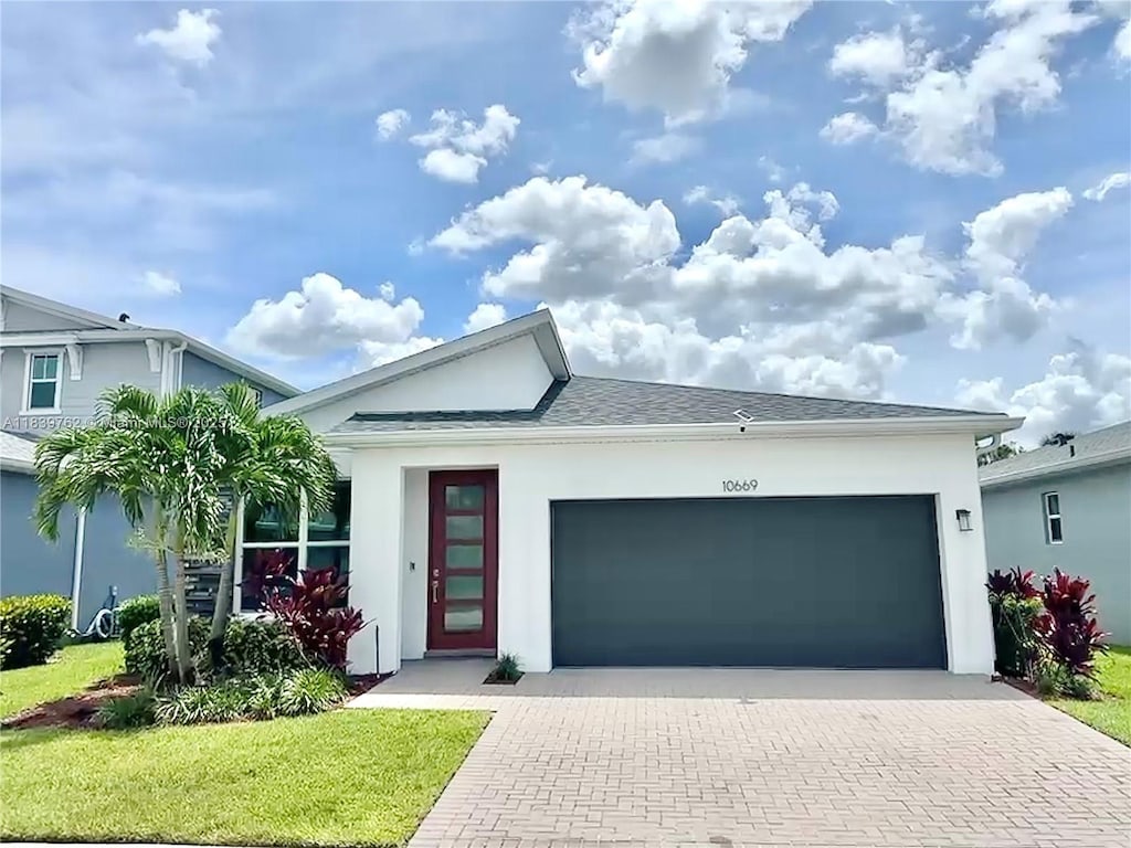 10669 SW Gloriana St, Port St Lucie, FL 34987 - view of front of home with decorative driveway, an attached garage, stucco siding, a front yard, and roof with shingles