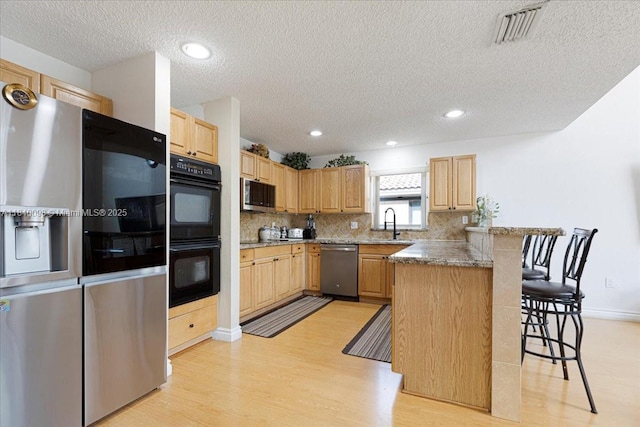 13063 NW 11th Ct, Sunrise, FL 33323 - kitchen featuring appliances with stainless steel finishes, a breakfast bar area, a peninsula, light wood-style flooring, and a textured ceiling