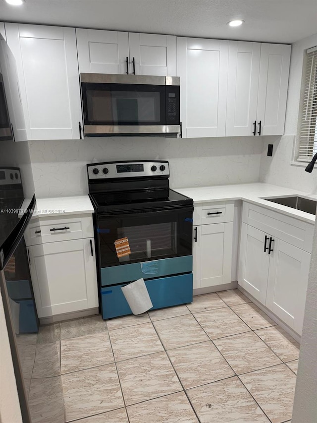3860 W 11th Ln, Hialeah, FL 33012 - kitchen with stainless steel microwave, black electric range, white cabinetry, light countertops, and recessed lighting