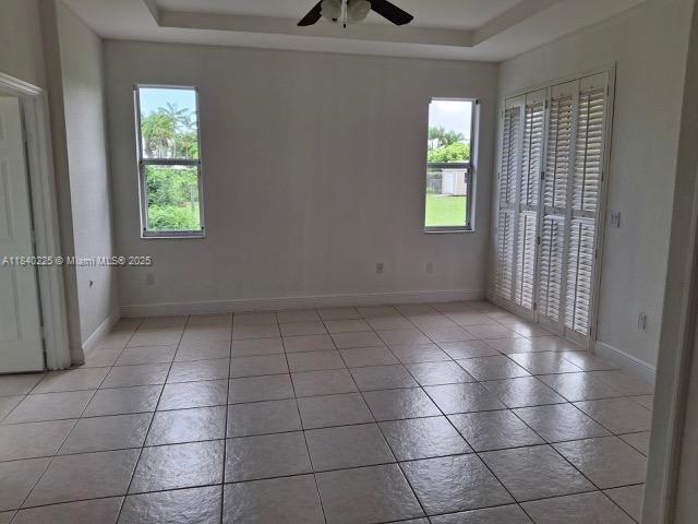 16961 SW 213th Ln, Miami, FL 33187 - unfurnished bedroom with a tray ceiling, tile patterned flooring, and a ceiling fan