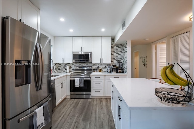 7625 NW 79th Ave Unit 101, Tamarac, FL 33321 - kitchen featuring appliances with stainless steel finishes, light wood finished floors, backsplash, white cabinetry, and recessed lighting