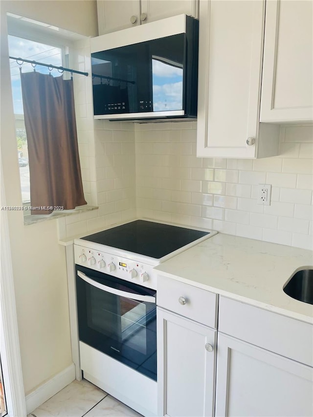 3401 SW 11th St Unit 1B, Miami, FL 33135 - kitchen with white range with electric cooktop, stainless steel microwave, decorative backsplash, white cabinetry, and light stone counters