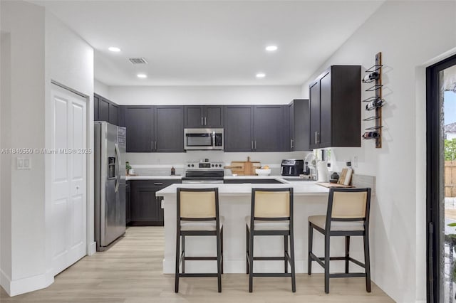 25009 SW 108th Ave, Homestead, FL 33032 - kitchen featuring stainless steel appliances, a peninsula, light wood-style floors, light countertops, and a kitchen breakfast bar